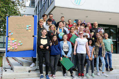 Die Gruppe der Teilnehmenden steht vor dem Schulgebäude neben einer blauen Pinnwand auf der einige Ergebnisse des Workshops gepinnt sind