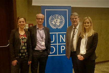 Vier Personen vor Aufsteller mit Logo des Entwickllungsprogramms der Vereinten Nationen (UNDP)