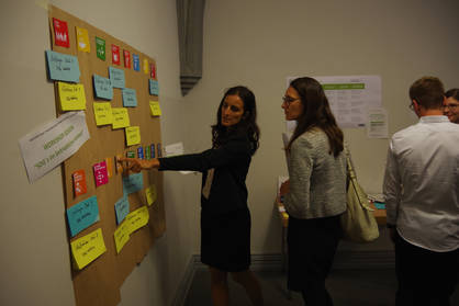 Zwei Frauen stehen vor einem Poster, auf dem Post-Its aus dem Workshop "SDGs im betrieblichen Kontext abgebildet sind"